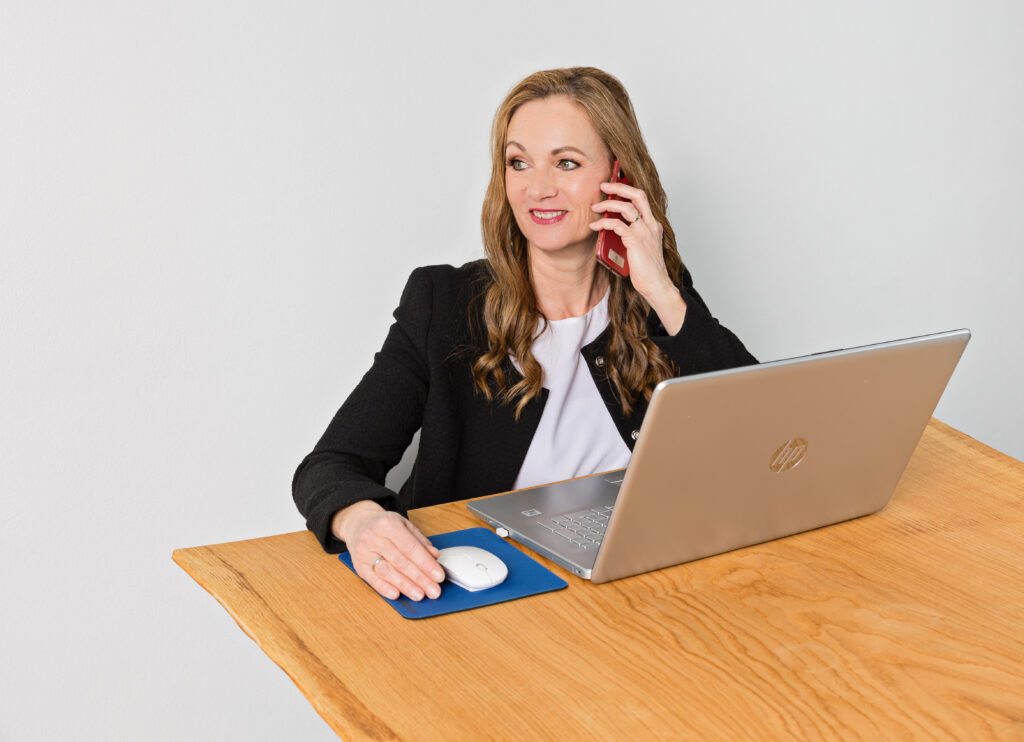 Frau sitzt am Schreibtisch und teleofniert mit Handy in der Hand